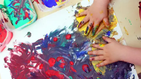 A small child's hands covered in paint and smearing paint all over a piece of paper.