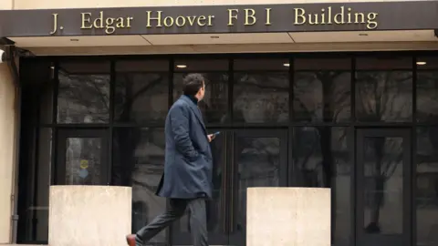 A man with his back to the camera walks outside the J Edgar Hoover FBI building