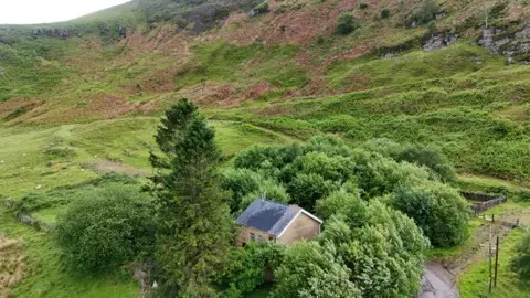 Paul Fosh Auctions A house is pictured surrounded by trees at a bottom of a mountain