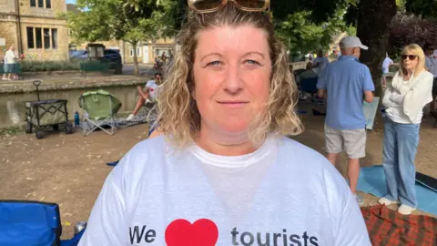 Charlotte Joynes wears a "We love tourists" T-shirt and has sunglasses on her head. She has curly blonde hair to her shoulders.
