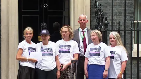 A group of women standing in front of 10 Downing Street wearing white t-shirts reading "Lobular Moon Shot Project". A man is standing behind them.