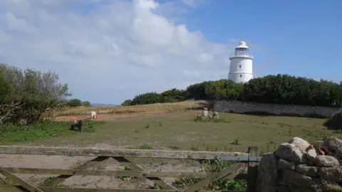 A view over a gate, across a field with the white St Agnes lighthouse through the field