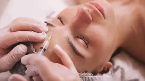 A generic image of a procedure, with a piece of equipment on a woman's forehead. She is lying down in the photo and her eyes are closed.