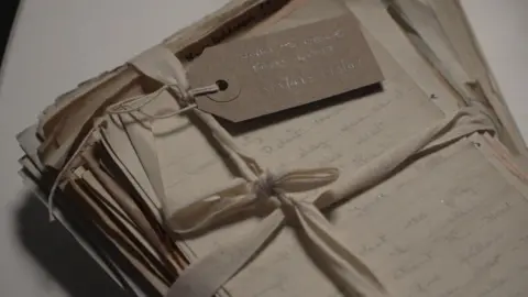 A stack of hand-written letters all kept together by a white bow tied around them.