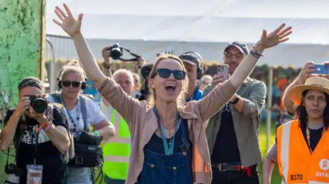 Getty Images Emily Eavis with her hands in the air on the first day of Glastonbury, 2024. She is wearing denim dungarees.