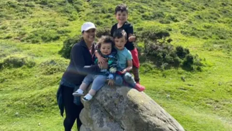 Michelle Campbell A woman is seen standing in a field with three boys sat on a rock.