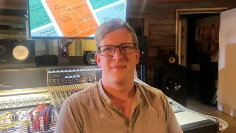 Photograph of Jamie Alsop form Voltalab Sound Studios in Rochdale. The image shows a mixing desk in the background.