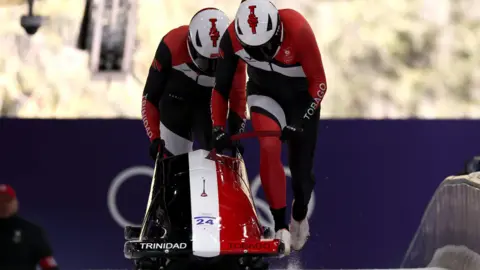 Getty Images Axel Brown and Aundre de John of Team Trinidad And Tobago compete in the Men's Two-Man Bobsleigh. They can be seen pushing their red‑and‑black sled at the start of a run.