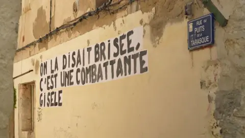 Slogan seperti ini pernah muncul di Avignon: "Mereka bilang dia hancur, dia seorang pejuang, Gisèle"