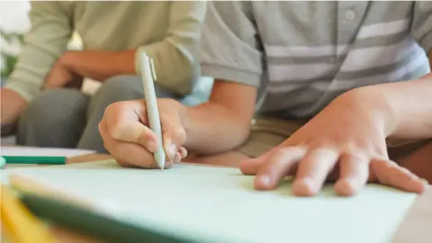 Getty Images An unidentified child writes on a board with a pen. An adult sits close behind them.