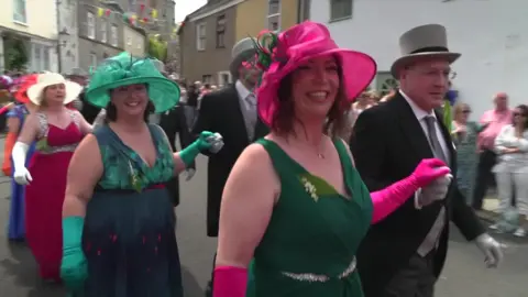 Women dressed in bright dresses and hats and men dressed in top hats and tails dance through Helston on Flora Day 