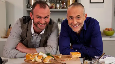  BBC/Andrew Hayes-Watkins Glynn Purnell and Michel Roux Junior leaning on a worktop, with food in front of them  on  chopping board