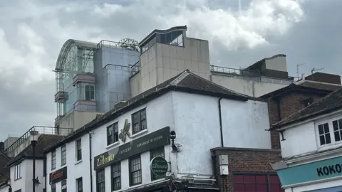 Julia Gregory / BBC A building made of several cream panels with a glass-panelled front.