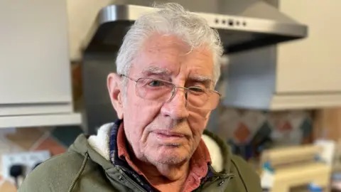Older man with white hair and glasses in a kitchen.
