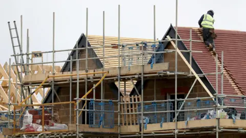 PA Media A house being constructed - showing a man climbing on a half-built roof, and sections of loose timber.
