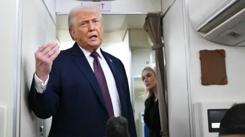 Donald Trump talking to press on Air Force One he is wearing a navy blue suit