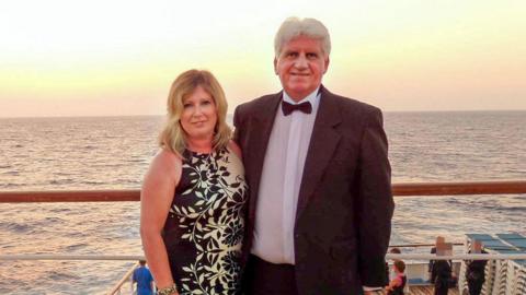 Susan Baird is pictured left and Gary Baird stands to her right. They are in formal wear on a boat.