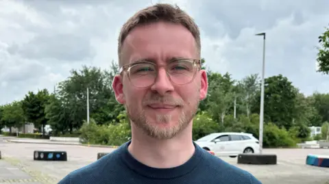 A picture of Fraser Stewart outside while wearing a blue sweatshirt and glasses. 