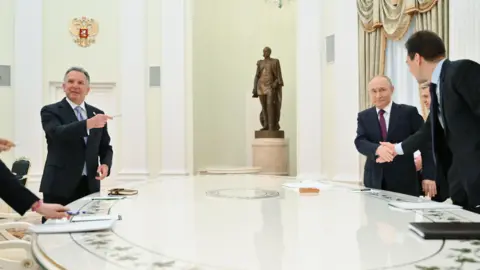 EPA Witkoff, who wears a suit and has short grey hair, points with a pen towards Putin, who also wears a suit and had short thinning grey hair, as they stand around a large white table at the Kremlin