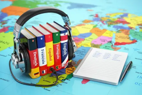 A number of foreign language books are on a map of the world beside a notebook and pen