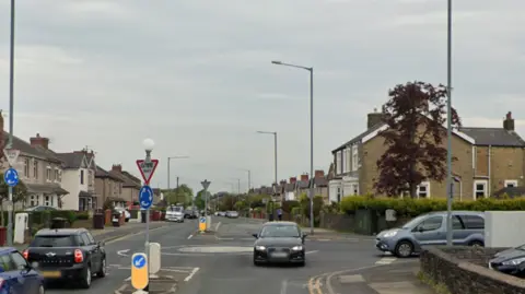 A Google image shows the roundabout on Brunshaw Road, Burnley, where Brownside Road joins it on the right-hand side. There are several cars in the image. The road is flanked by terraced houses. 