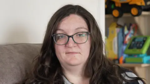 A woman with round glasses and long brown hair sitting on a sofa