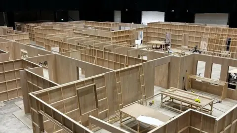 Adam Tomlinson Image shows a wooden set divided into different rooms. Building tools and ladders are included. 