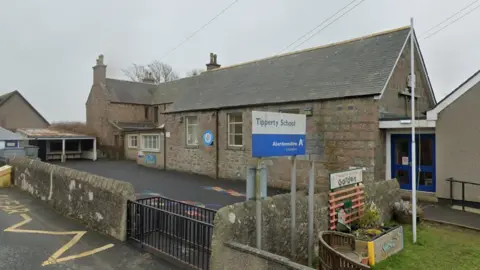 A blue and white sign reading "Tipperty School". There's a small playground in front of the main building. 