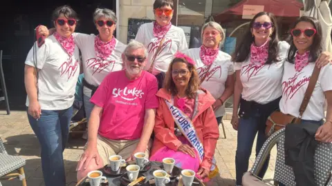 supplied An elderly man in a pink t-shirt poses with several younger women all wearing matching 'Dirty Dancing' t-shirts. Infront of them is a table full of coffees.