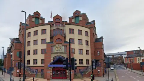 The exterior of Leeds Magistrates Court. A large modern red-brick building, with red front doors and traffic lights in front of it.