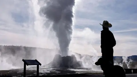 Getty Images A man is a cowboy hat and his dog are silhouetted in front of the steam coming from the Castle Geyser in Yellowstone National Park, Wyoming. 