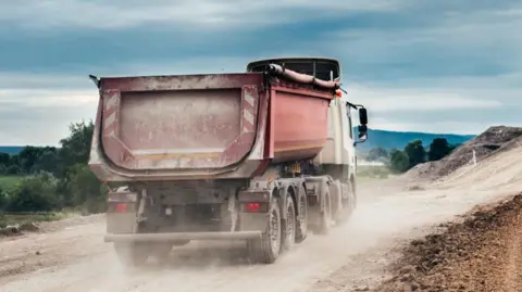 An industrial dumper truck driving on a dusty highway construction site.