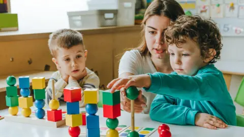 Two children and a woman are playing with colourful toys.