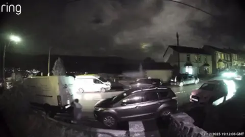Kevin James This images shows ring door bell footage of someone taking pictures of a work van while they walk past. The van is parked on the side of the road in a residential street. You can see the person holding their mobile phone towards the van. 