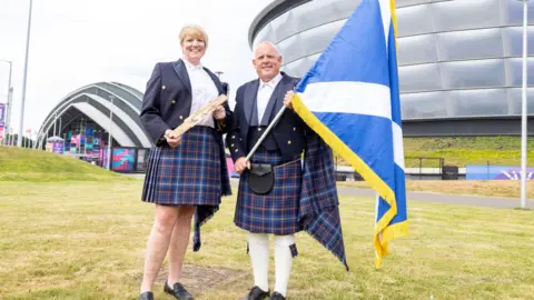 PA Media a man and woman in full Highland gear holding a scotland flag and baton outside the Hydro venue