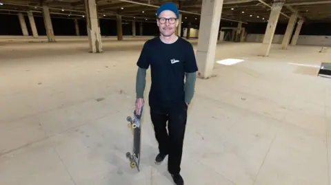 THRINGS Tim standing in the empty abandoned department store holding his skateboard