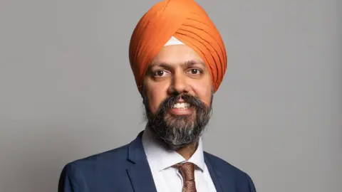 UK Parliament A headshot of a man with a greying beard wearing a blue suit and an orange turban.