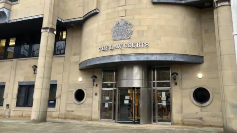 The front of Bradford Crown Court: a large light-stoned building with silver metal details and a sign above the door that reads: The Law Courts