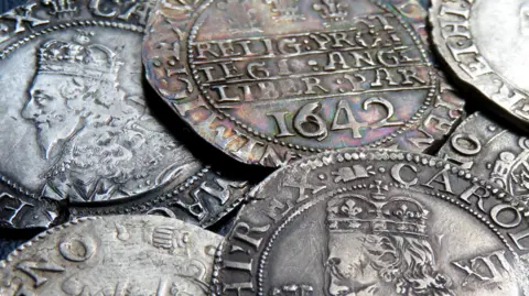 A close up image of several silver coins with clear markings. The profile of a king is stamped onto two of them. Another is dated 1642.