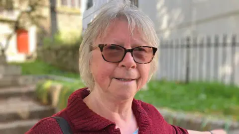 A woman with short blonde hair and glasses smiling at the camera
