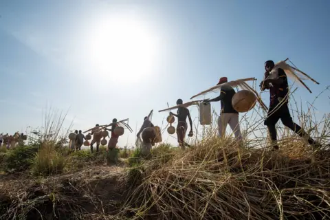 Sani Maikatanga A line of fishermen seen in silhouette walking with their nets and gourds.