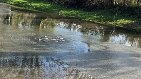 A drain in a road is overflowing and the road is flooded.