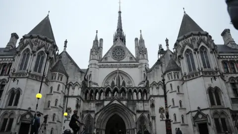 PA Media People gathering around the Royal Courts of Justice, a grand, gothic building with pointed roofs and arches, on a grey day