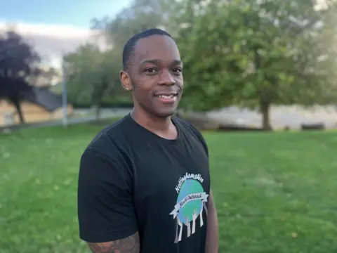 Romel Davis pictured outside the youth club in Bilborough while smiling. He is wearing a black shirt.