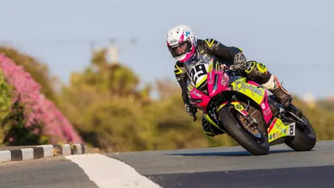 SOUTHERN 100 Naughton racing on the Billown Course. He is in Black and yellow leathers with a white helmet on a pink and yellow bike.