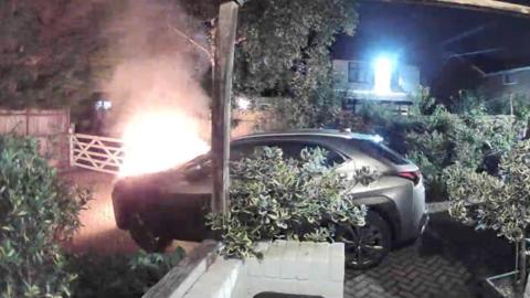 A car with the bonnet on fire in a driveway