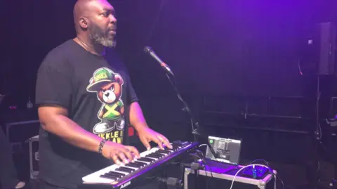 Kaidi Tatham playing a keyboard on stage during the rehearsal of North Star. He is wearing a black t-shirt with a bear on the front.