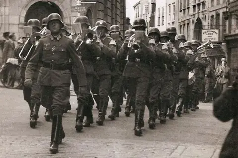 German soldiers in uniform, some playing musical instruments, march in front of the Lloyds bank building in St Peter Port