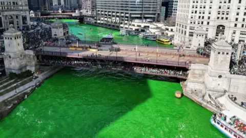 The Chicago flows through the city, under a bridge and passes large skyscrapers. The river is green after crews used a vegetable based dye in celebration of St. Patrick's Day.