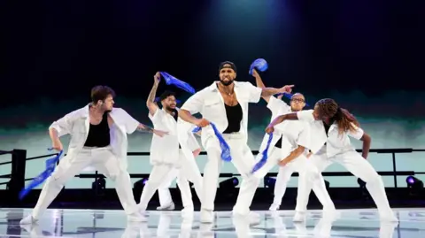 Andrew Milligan/PA A shot of six dancers on stage, they're dressed in white and flailing blue cloths around